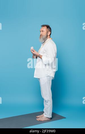 Die ganze Länge eines barfuß-Guru-Mentors meditiert mit Selenitstein auf blauem Hintergrund Stockfoto