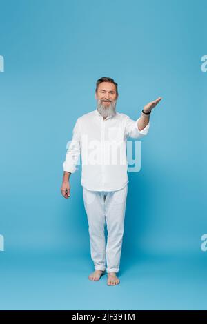 Die ganze Länge des bärtigen Barfußmanns in weißen Kleidern zeigt mit der Hand auf blau Stockfoto