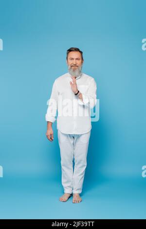 Die ganze Länge des Meister-Gurus in weißen Kleidern zeigt eine Segensgeste auf Blau Stockfoto