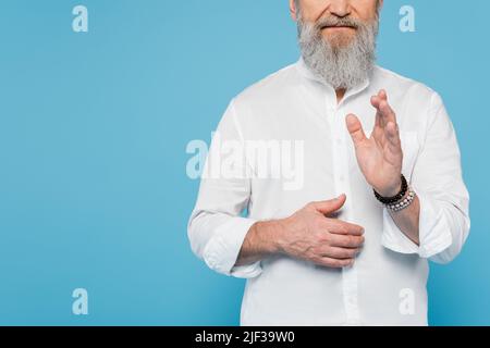 Beschnittene Ansicht des Gurustrainers mit grauem Bart, die auf blau isolierte Segensgeste zeigt Stockfoto