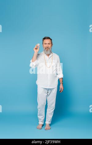 In voller Länge barfuß Yoga-Lehrer hält Selenit Kristall auf blauem Hintergrund Stockfoto