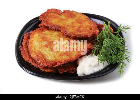 Kartoffelpfannkuchen mit Sauerrahm und Dill auf einem schwarzen Porzellanteller Stockfoto