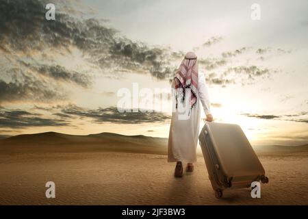 Rückansicht eines arabischen Mannes mit Keffiyeh, der mit einem Koffer unterwegs war, um in der Wüste zu reisen Stockfoto
