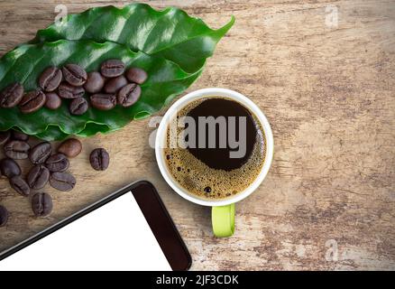 Tasse Kaffee und Smartphone mit Kaffeebohnen auf Holztischhintergrund. Platz kopieren Stockfoto