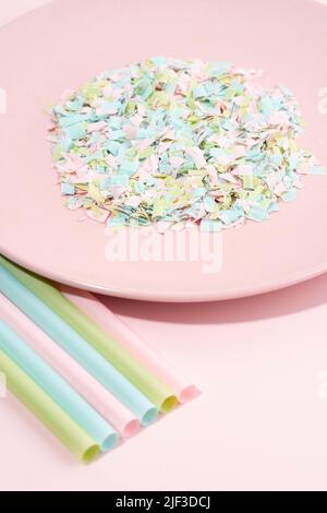 Trinkhalme und Teller voller Mikroplastik auf rosa Hintergrund. Auswirkungen von Mikroplastik auf die Lebensmittelkette. Die Idee der Mikroplastik Verschmutzung. Stockfoto