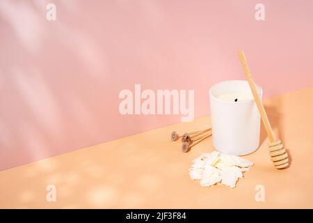 Duftkerze aus biologischem Sojawachs, Docht in einem weißen Keramikglas auf einem beige-rosa Hintergrund. Trendy diy, handgemachtes Konzept. Minimalismus. Isometrische Projektion Stockfoto