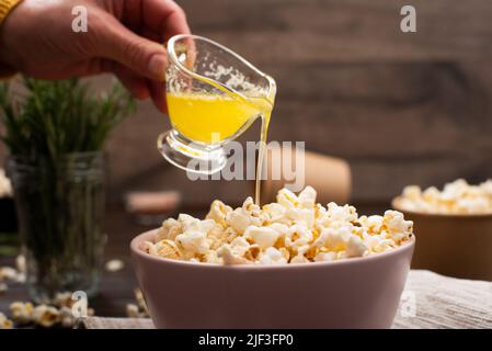 Geschmolzene Butter wird in einer Tonschüssel auf dem Küchentisch auf Popcorn gegossen Stockfoto