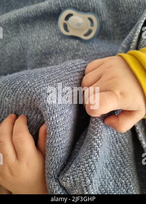 Babys Hand über eine blaue Decke. Sentimentaler Moment mit einem ruhenden Kleinkind. Kleine Hand eines neugeborenen Sohnes. Baby Schnuller im Hintergrund. Stockfoto