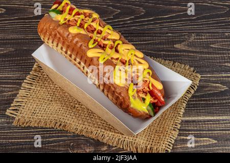 Hot Dog mit Wurst in einer Papierbox mit Tomaten und Mais, Chilischoten, Gurken und Salat. Auf einem roten Hintergrund. Fastfood. Kopierplatz Stockfoto