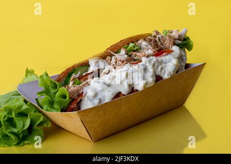 Hot Dog mit Wurst in einer Papierbox mit Tomaten und Mais, Chilischoten, Gurken und Salat. Auf einem roten Hintergrund. Fastfood. Kopierplatz Stockfoto