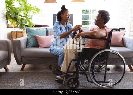 afroamerikanischer Arzt, der die Hand eines älteren Patienten in einer Sauerstoffmaske hält und im Rollstuhl sitzt Stockfoto