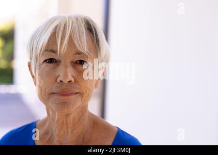 Nahaufnahme eines lächelnden asiatischen Senioren mit kurzen Haaren an der weißen Wand im Pflegeheim Stockfoto