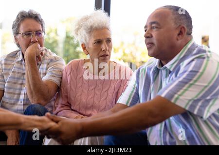 Multirassische Senioren schauen auf den Mann, der die Hände der Frau hält und sie in einer Gruppentherapie tröstet Stockfoto