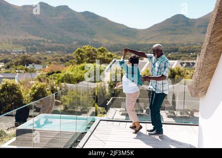 Ältere Freunde aus verschiedenen Rassen tanzen im Sommer auf dem Balkon gegen den Berg Stockfoto