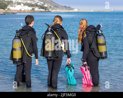 Taucher, die am Strand trainieren und ihren Tauchgang planen, weisen auf das Meer hin, das ihr komplettes Tauchkit trägt Stockfoto