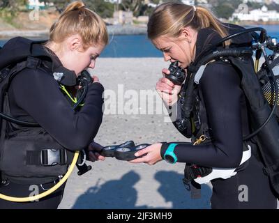 Taucher, die am Strand trainieren und zwei Personen vor dem Tauchgang ihren Buddy-Check machen. Manometer prüfen Stockfoto