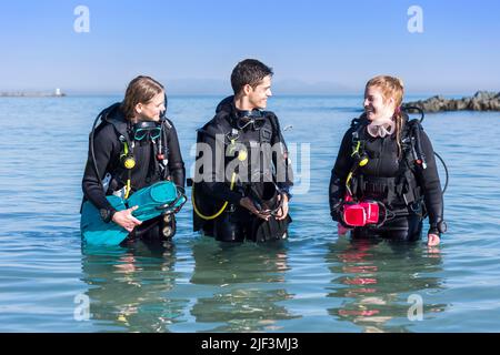 Glückliche Taucher, die nach einem Tauchgang am Ufer aus dem Meer laufen Stockfoto