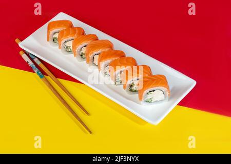 Nigiri Sushi Sets, Uramaki, Kalifornien, Philadelphia, auf einem weißen Teller. In der Nähe von Ingwer und Wasabi. Sojasauce in einer weißen Schüssel. Auf farbigem Hintergrund. Co Stockfoto