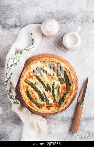 Quiche. Hausgemachter Spargelkuchen oder Quiche mit Käse, Pecorino, Speck und Spinat auf grauem, hellem Tischhintergrund aus Beton. Spargel und Käsetorte. Stockfoto