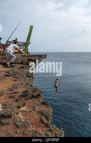 Ein Mann springt von der Klippe und springt auf den South Point der Big Island, während seine Freunde auf ihn schauen. Stockfoto