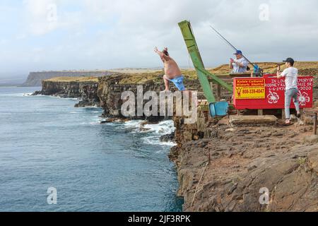 Ein Mann springt von den Klippen des South Point der Big Island ins Meer, während seine Freunde in Hawaii Fotos machen Stockfoto