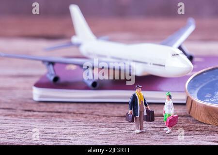 Miniaturreisende, die auf dem Boden und dem Flugzeug stehen, Kompass und Reisepass auf einem Holztisch. Foto im Retro-Farbbildstil. Draufsicht mit c Stockfoto