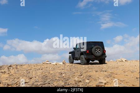 Geländewagen fahren durch die Wüste vor einem blauen Himmel mit Wolken Stockfoto