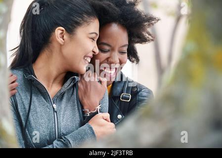 Zwei fröhliche Freunde umarmen sich gegenseitig und lachen während eines Ausflugs in den Park. Eine glückliche junge Frau umarmte ihren Freund liebevoll. Zwei Freunde Stockfoto