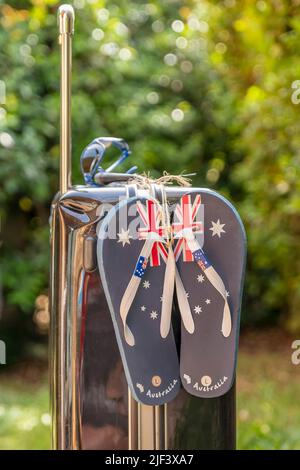 Flip Flops mit der australischen Flagge, die mit einer Schnur an einen Reisewagen gebunden ist, auf einem grünen unscharfen Hintergrund und Bokeh-Lichtern Stockfoto