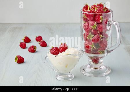 Rote Himbeeren in einem Glas-Soße-Boot mit Creme und in einem Glas-Kelch Stockfoto