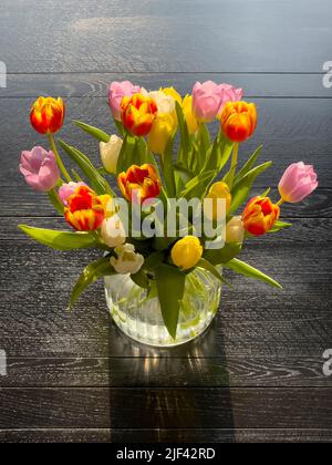 Farbenfrohe Tulpenblumen in einer Glasvase auf einem schwarzen Holztisch Stockfoto