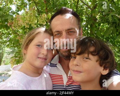 Ein bärtiger Vater umarmt seine Tochter und seinen Sohn Stockfoto