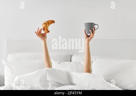 Frau mit Kaffee und Croissant, die im Bett lag Stockfoto
