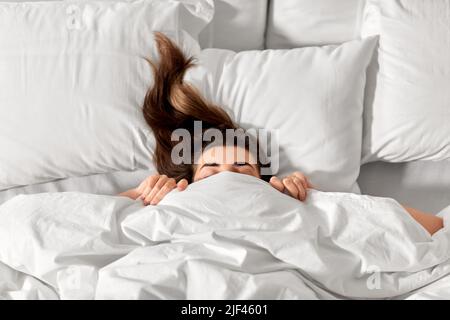 Frau, die im Bett unter einer weißen Decke oder Bettdecke liegt Stockfoto