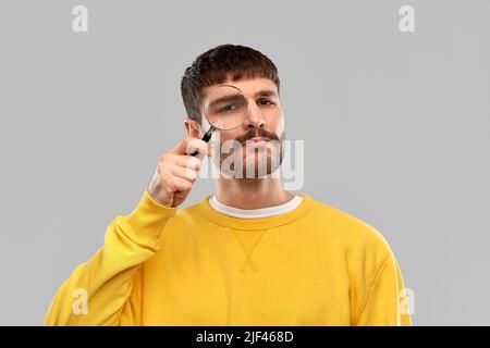 Mann im gelben Sweatshirt mit Lupe Stockfoto