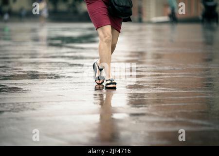 Eine Frau in Sandalen wird am 29. Juni 2022 durch flache Regenpfützen in der Altstadt von Warschau, Polen, laufen sehen. Stockfoto