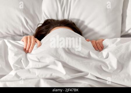 Frau, die im Bett unter einer weißen Decke oder Bettdecke liegt Stockfoto