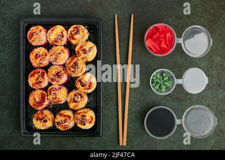 Gebackene Lachs- und Aalrollen in einem Plastiktablett zum Mitnehmen, Gläser mit Ingwer, Wasabi und Sojasauce, orientalische Küche Stockfoto