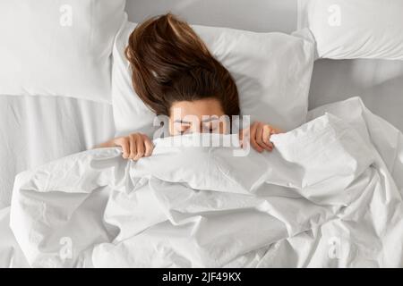 Frau, die im Bett unter einer weißen Decke oder Bettdecke liegt Stockfoto