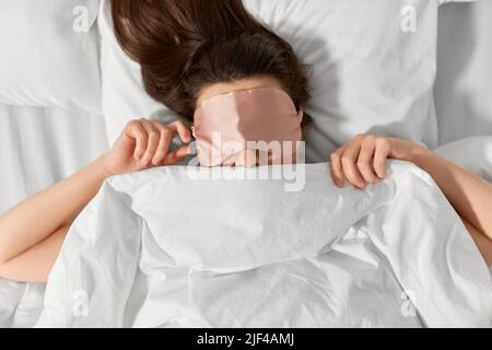 Frau mit Augenschlafmaske im Bett unter der Decke Stockfoto