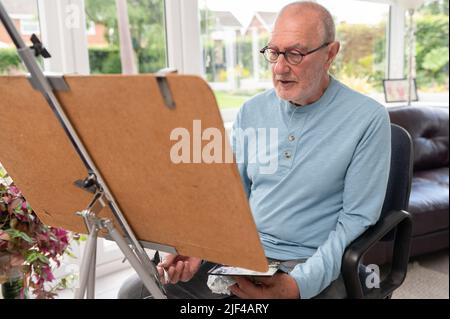 Umweltportrait eines älteren Mannes, der in seinem Atelier mit Aquarellen malte Stockfoto