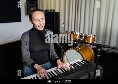 Junge Japanerin oder Europäerin, die Lied auf Mikrofon singt und elektronisches Klavier spielt Stockfoto