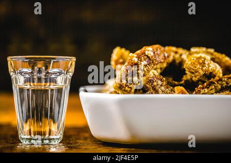 Cachaça oder Pinga, ist der in Brasilien hergestellte Zuckerrohrschnaps, der mit knusprigen Schweinefleischspülungen oder gebratenem Speck, Schweinefleisch serviert wird. Stockfoto