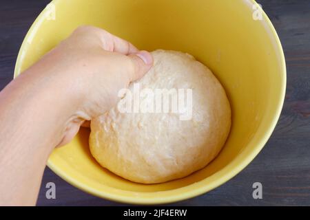 Die Hand des Mannes, der den kneteten Teig in eine Schüssel legt, damit er vor dem Backen aufgehen kann Stockfoto