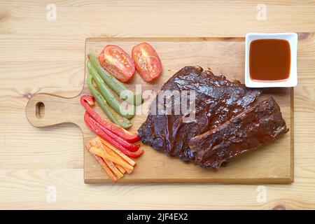 Köstliche gegrillte Schweinsrippen mit gegrilltem Gemüse auf einem Schneidbrett Stockfoto