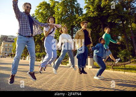 Fröhliche, aufgeregte, multiethnische Freunde, die gemeinsam Freizeit verbringen, springen und Spaß haben Stockfoto