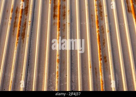 Der Hintergrund des rostigen Metallmaterials, das an der Decke einer Fabrik in den Paneelen mit den senkrechten Linien montiert ist Stockfoto