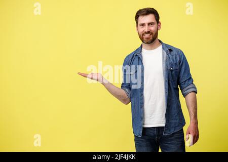 Lächelnder Mann steht auf gelbem Hintergrund und zeigt seinen Finger an einem leeren Ort zur Seite Stockfoto