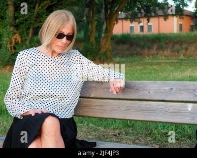 Ältere Dame, die im Sommer in der Nähe des Flussufers im Park entspannt und eine Sonnenbrille trägt Stockfoto