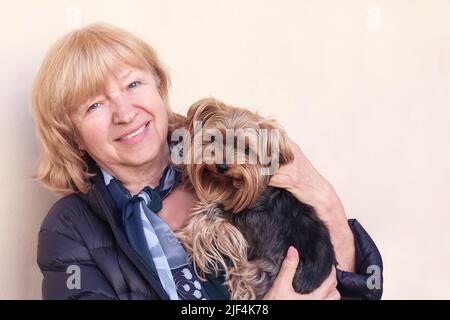 Porträt einer schönen, fröhlichen, lächelnden eligen Frau, die ihren kleinen yorkshire Terrier-Hund im Freien umarmt. Stockfoto